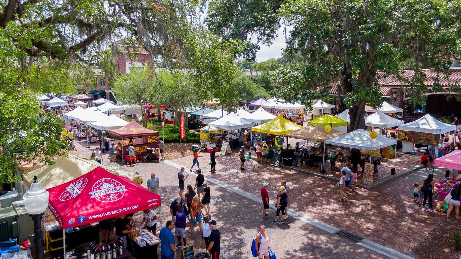Crowds browsing vendor tents at the Windermere farmers market on brick streets